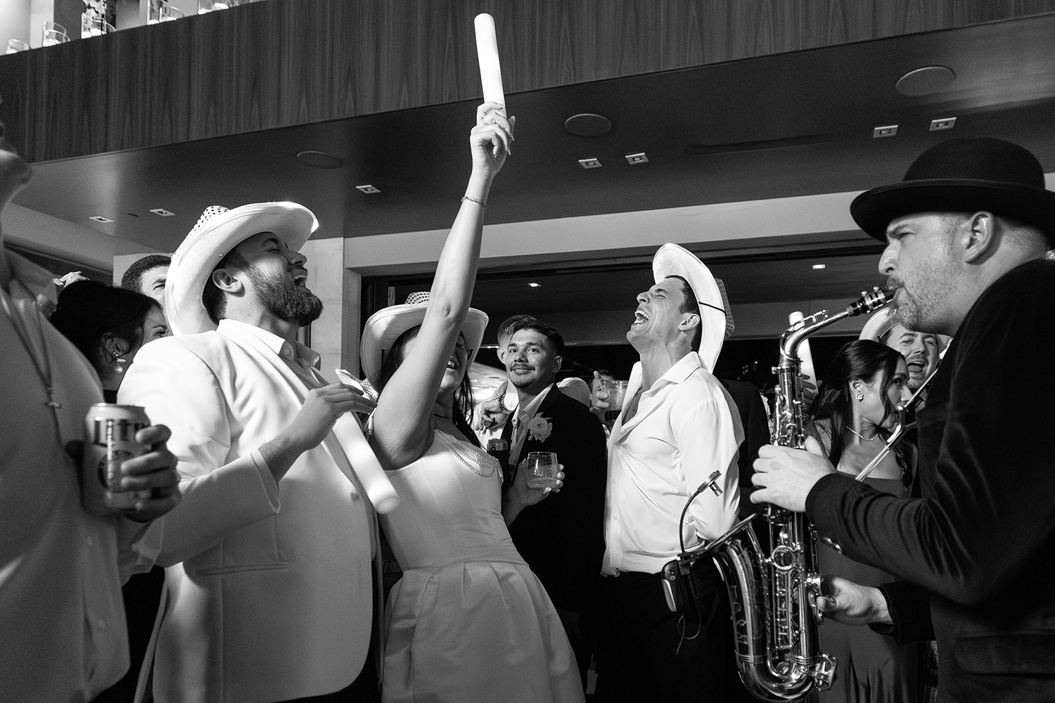 DJ vs band hybrid celebration: bride with arm raised next to her groom, surrounded by guests and Matt Thelen on live saxophone at a Dallas wedding reception